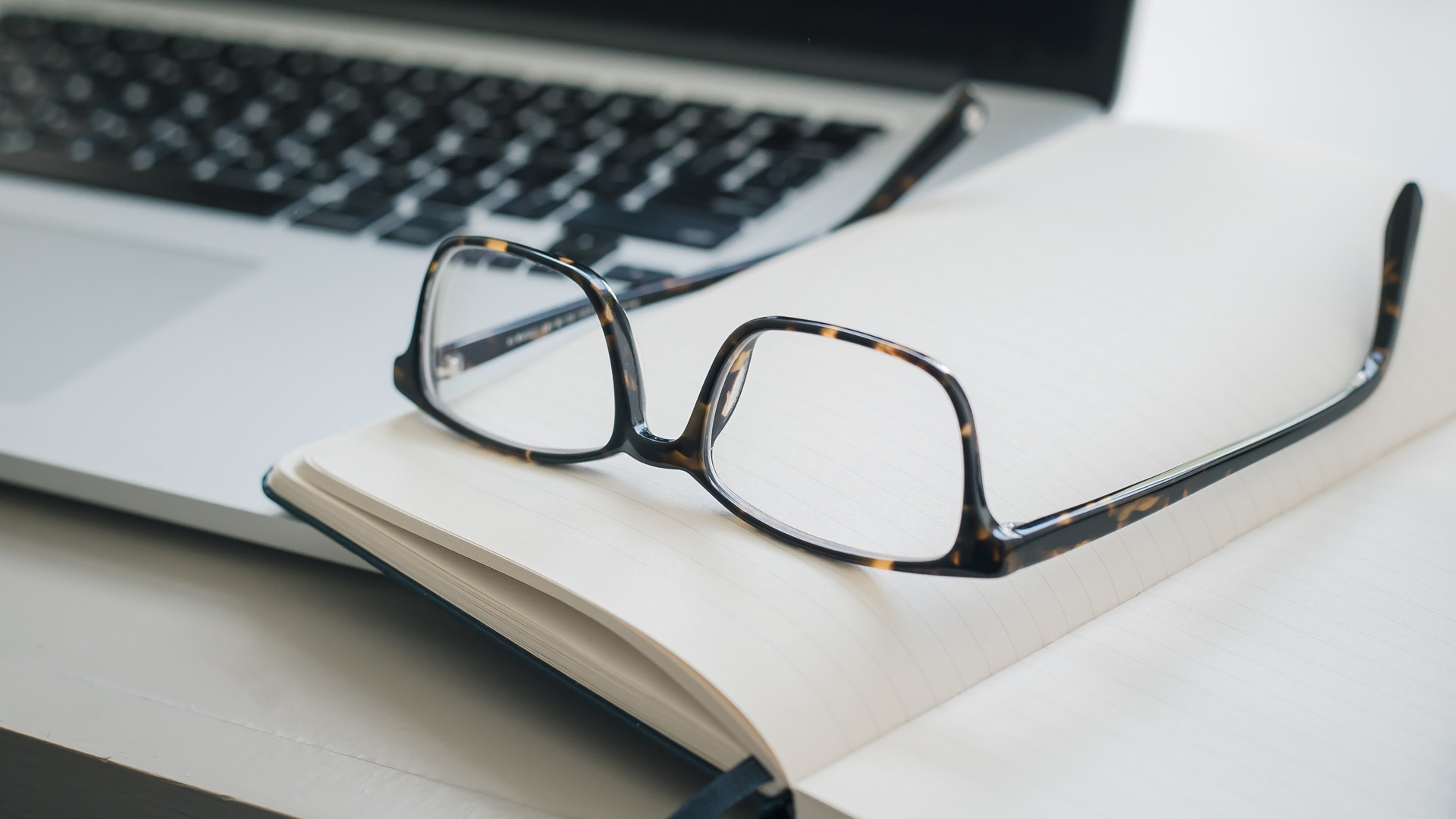 Glasses resting on a notebook and laptop